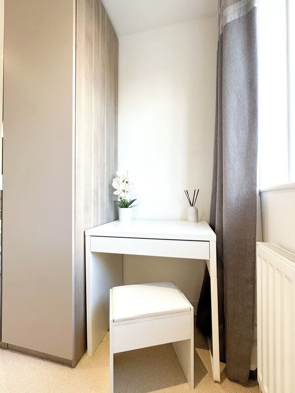 A corner room with a white desk, a small bench, a potted plant, and a radiator.