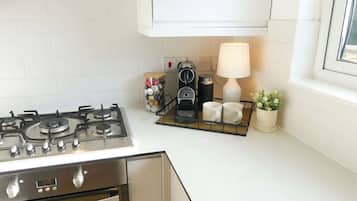 A kitchen with a gas stove, a coffee maker, a lamp, and a window.