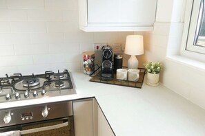 A kitchen with a gas stove, a coffee maker, a lamp, and a window.