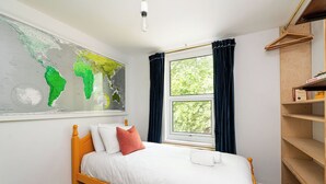 A bedroom with a bed, a map on the wall, a window with curtains, and a wooden shelf. - Comfortable 3BR Townhouse for 6 (London)