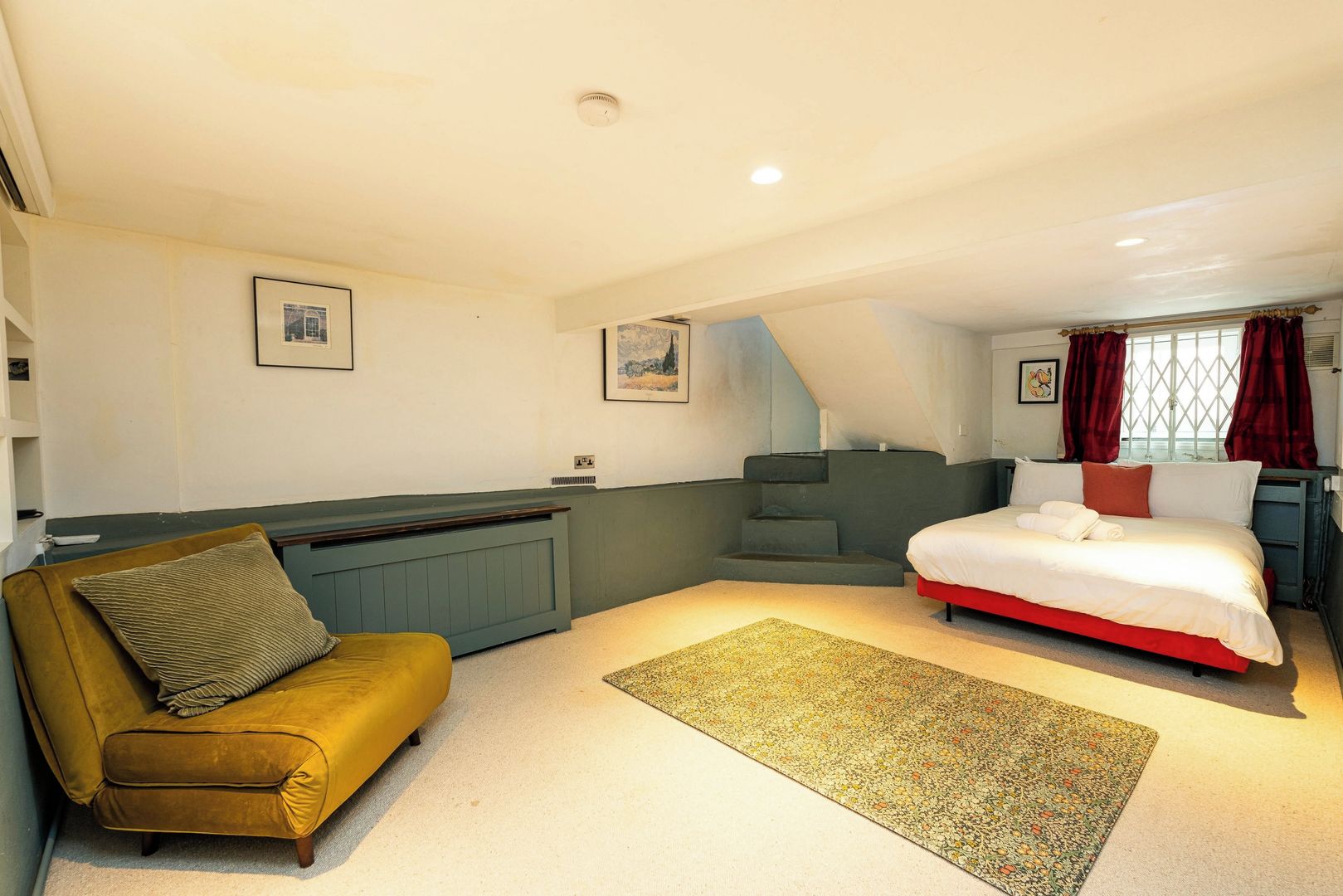 A bedroom with a bed, a sofa, a radiator, and a staircase.