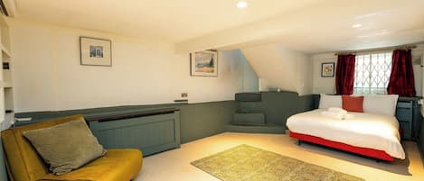 A bedroom with a bed, a sofa, a radiator, and a staircase.