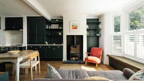 A cozy living room with a fireplace, a dining area with a wooden table, and a kitchen with dark green cabinets. - Comfortable 3BR Townhouse for 6 (London)