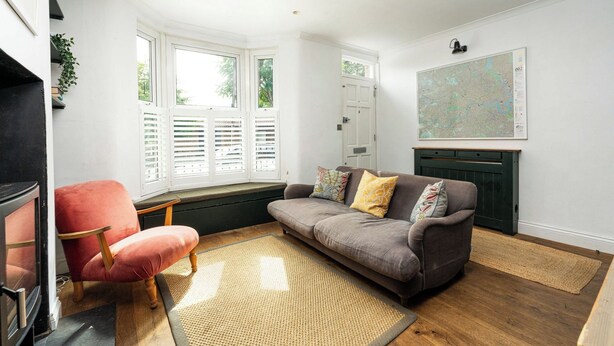 A living room with a sofa, a red chair, a fireplace, and a large window with shutters. - Comfortable 3BR Townhouse for 6 (London)