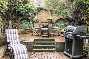 A patio with a grill, two chairs, and a striped chair. - Stunning 4 Bedroom Home w/Garden in Fulham (Greater London)