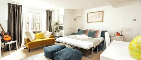 A modern bedroom with a bed, a sofa, a desk, and a guitar.