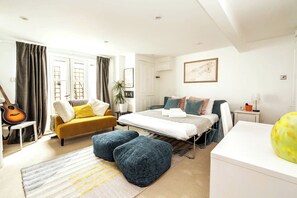 A modern bedroom with a bed, a sofa, a small table, and a guitar. - Stunning 4 Bedroom Home w/Garden in Fulham (Greater London)