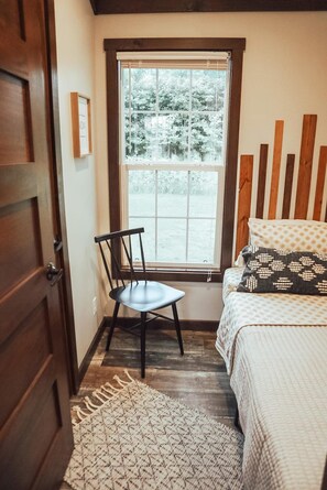 Un dormitorio con cama, una silla, ventana y puerta.