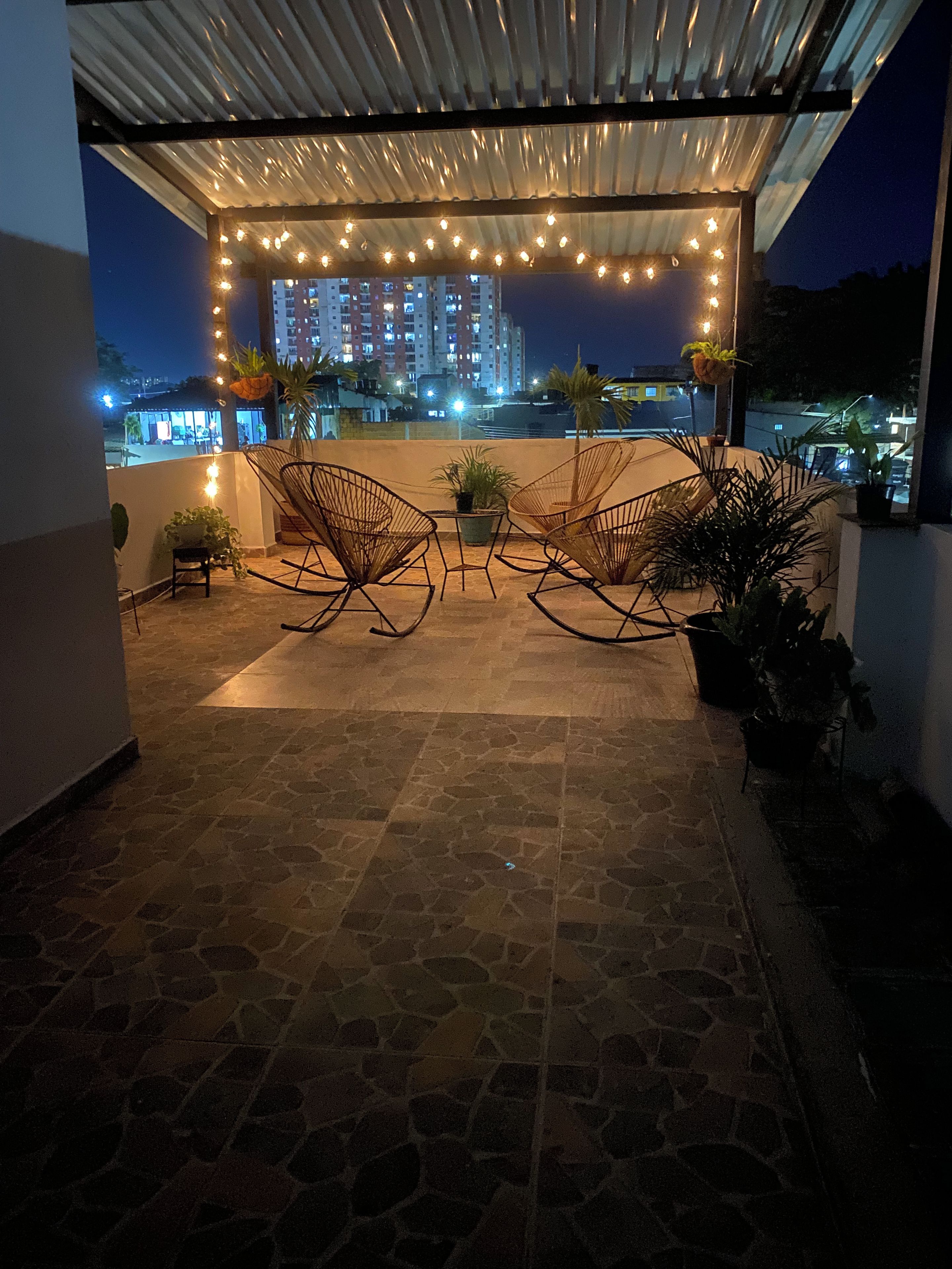 An outdoor patio area with stone flooring, two rocking chairs, potted plants, and string lights.