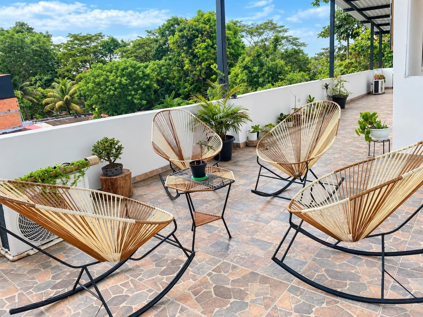Una terraza en la azotea con sillones de mimbre, plantas en macetas y una pequeña mesa.