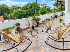 A rooftop terrace with wicker rocking chairs, potted plants, and a small table.