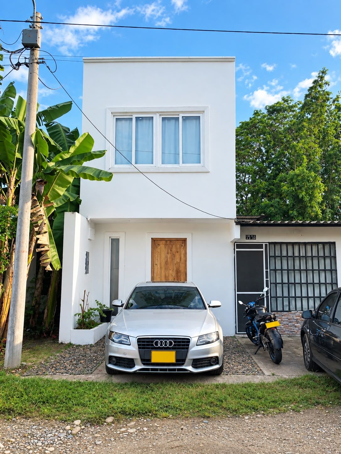Un edificio moderno de dos pisos con fachada blanca, un garaje para un coche y un auto plateado estacionado al frente.