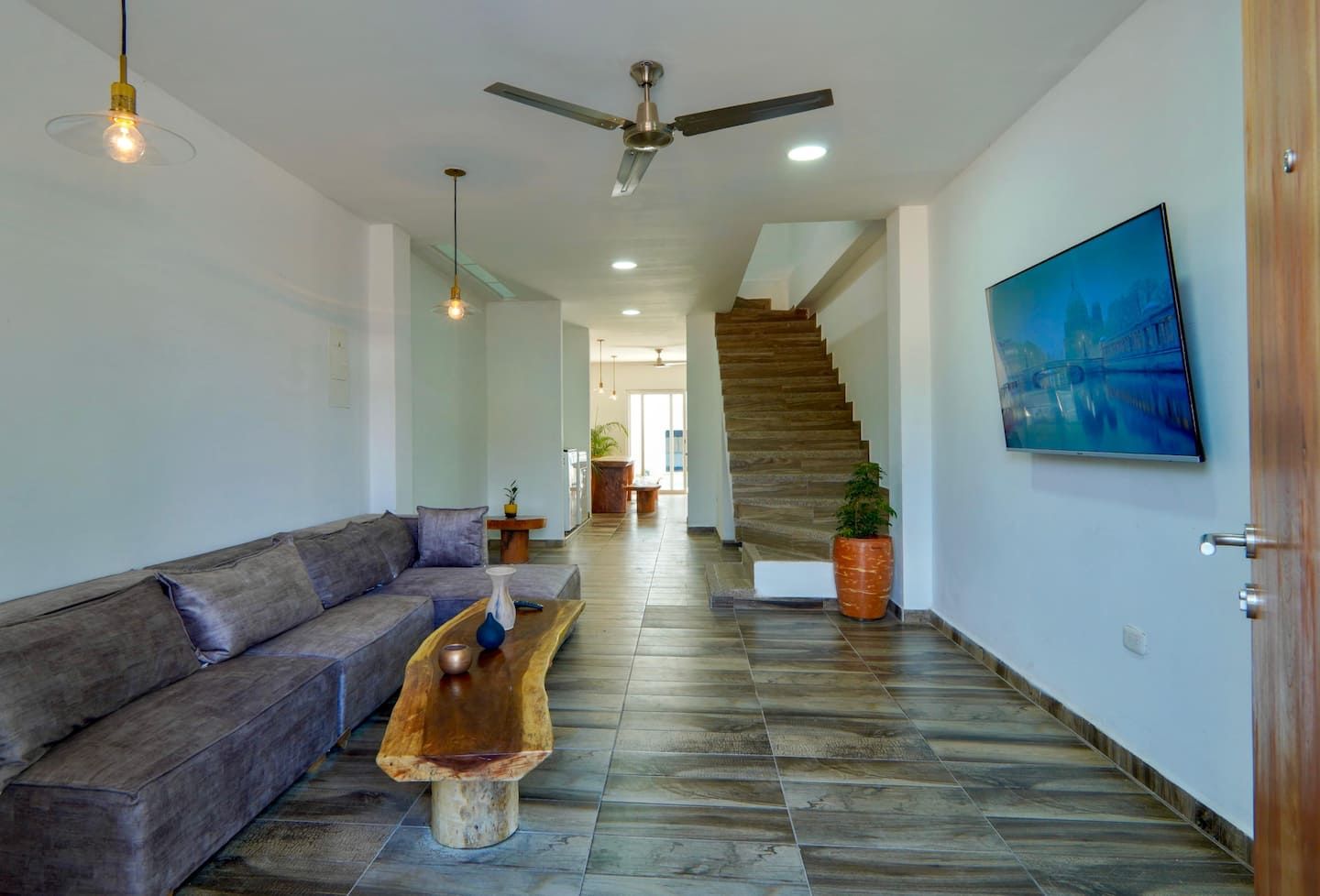 A modern living room with a sofa, a wooden coffee table, a ceiling fan, and a staircase leading to another room.