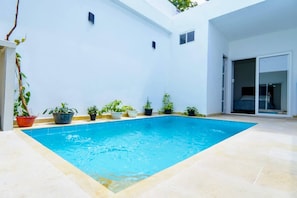 Una piscina circondata da vasi con piante, un muro bianco e una porta che conduce a una stanza.