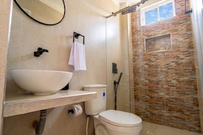 Un bagno con un lavandino bianco grande, un water e una zona doccia con parete in pietra.