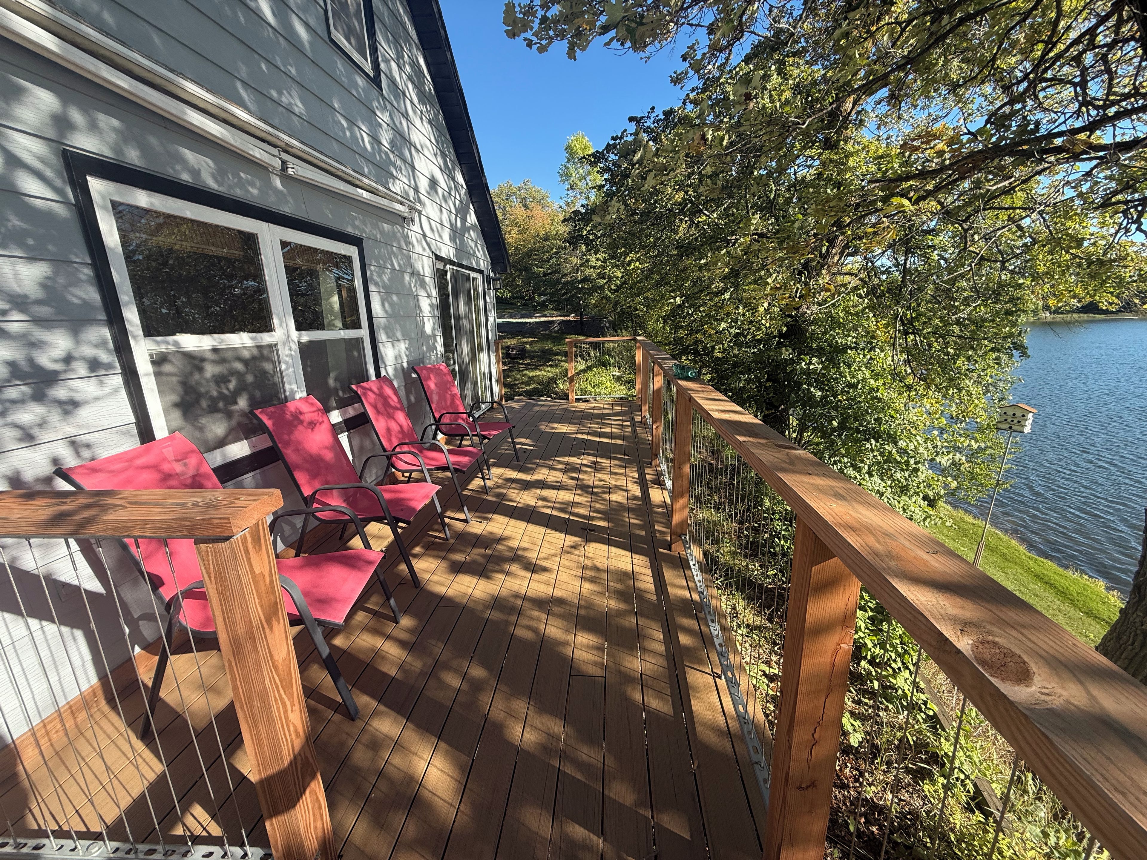 A wooden deck with red chairs and a railing overlooking a lake.