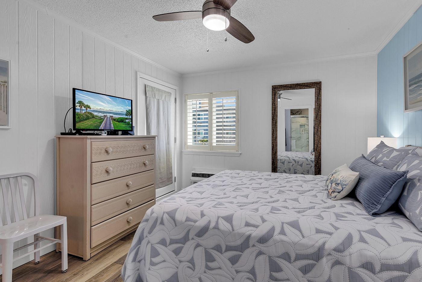 A bedroom with a bed, dresser, television, and a ceiling fan.