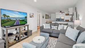 A modern living room with a flat-screen TV, grey sofas, and a kitchen in the background. - Oceanfront Shore Dr Condo w/ Pools & Beach Access (Myrtle Beach)