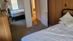 Een slaapkamer met een bed, een houten garderobe, een spiegel en een deur naar een andere kamer.