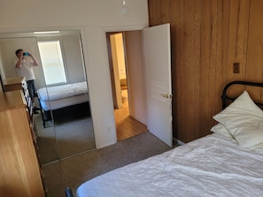 Quarto com cama, guarda-roupa de madeira, espelho e porta que dá para outro cômodo.