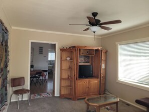 A living room with a ceiling fan, a wooden entertainment center, a glass coffee table, and a dining area with a table and chairs.