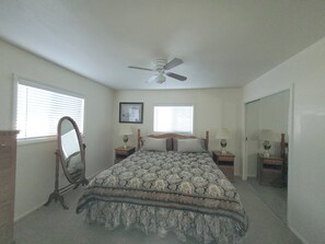 A bedroom with a bed, two bedside tables, a ceiling fan, and two windows with blinds.