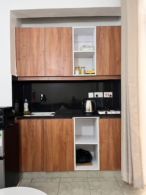 A compact kitchen with wooden cabinets, a black countertop, and a built-in shelf unit. - Cosy, homely haven made just for you! (Nairobi)