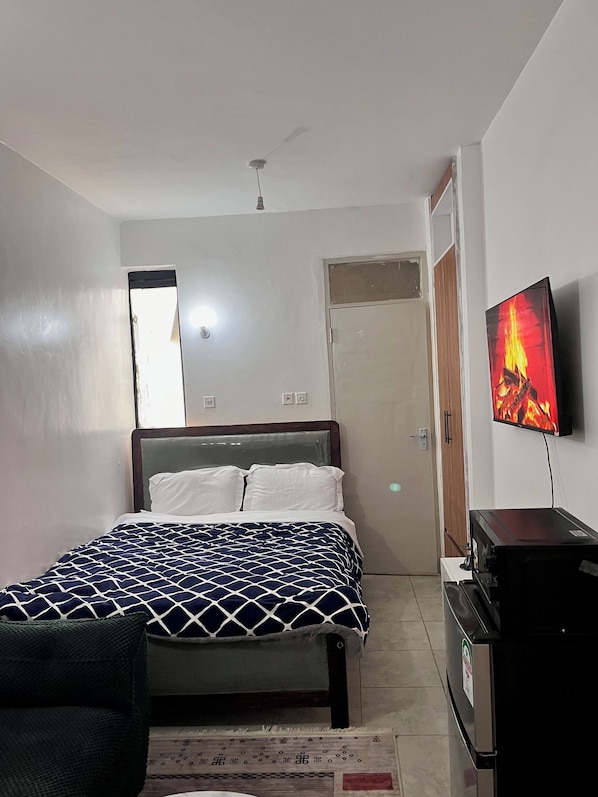 A bedroom with a bed, a television, a desk, and a door. - Cosy, homely haven made just for you! (Nairobi)