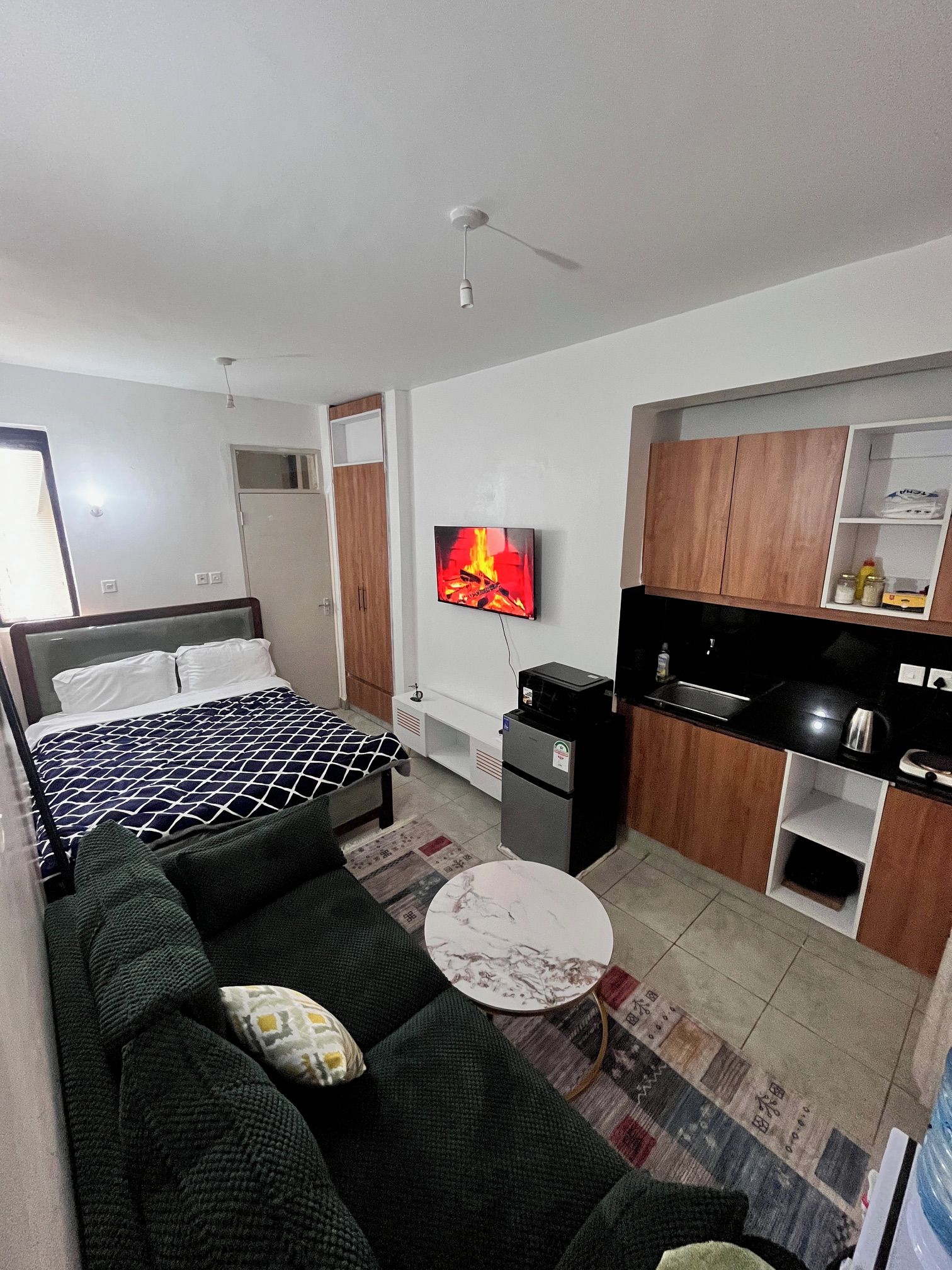 A modern hotel room with a bed, sofa, TV, kitchenette, and a small dining area.