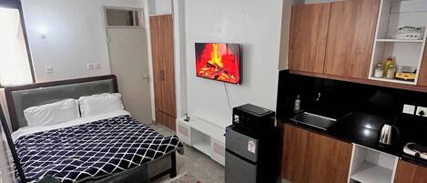 A modern hotel room with a bed, sofa, TV, kitchenette, and a small dining area.