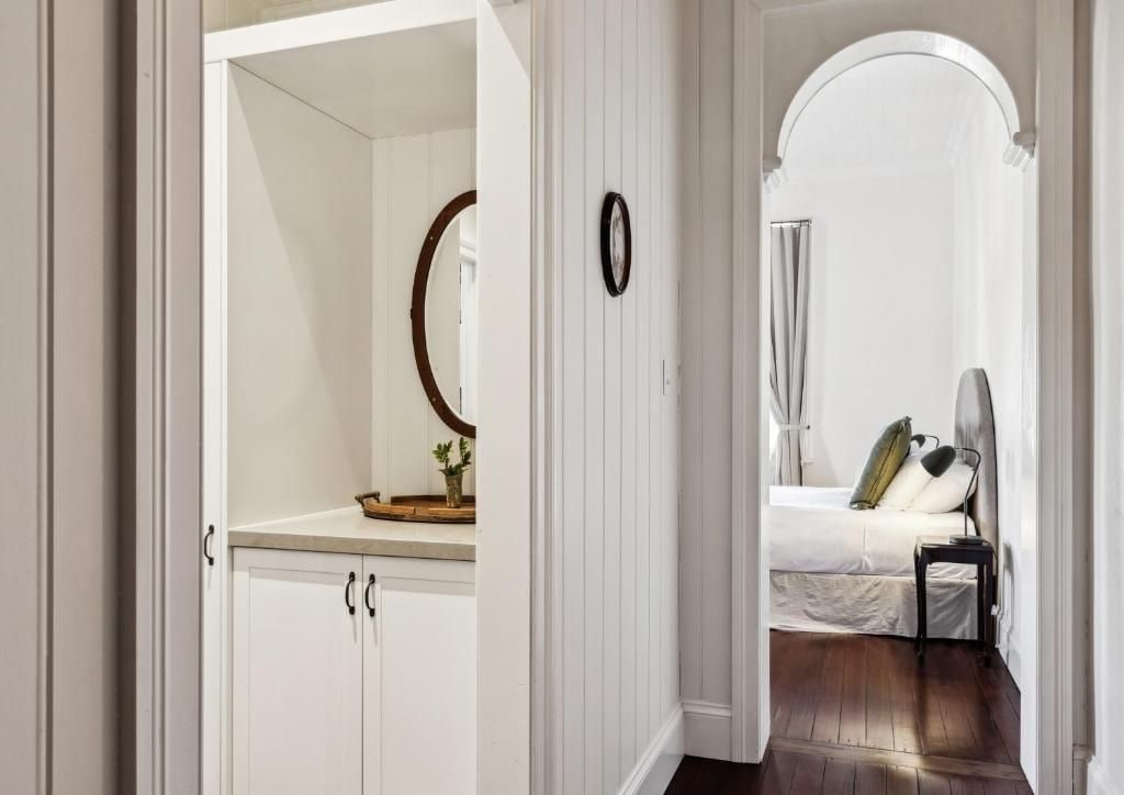 Un dormitorio con cama, mesita de noche y espejo. Hay una puerta que da a un baño con ducha y toallero.