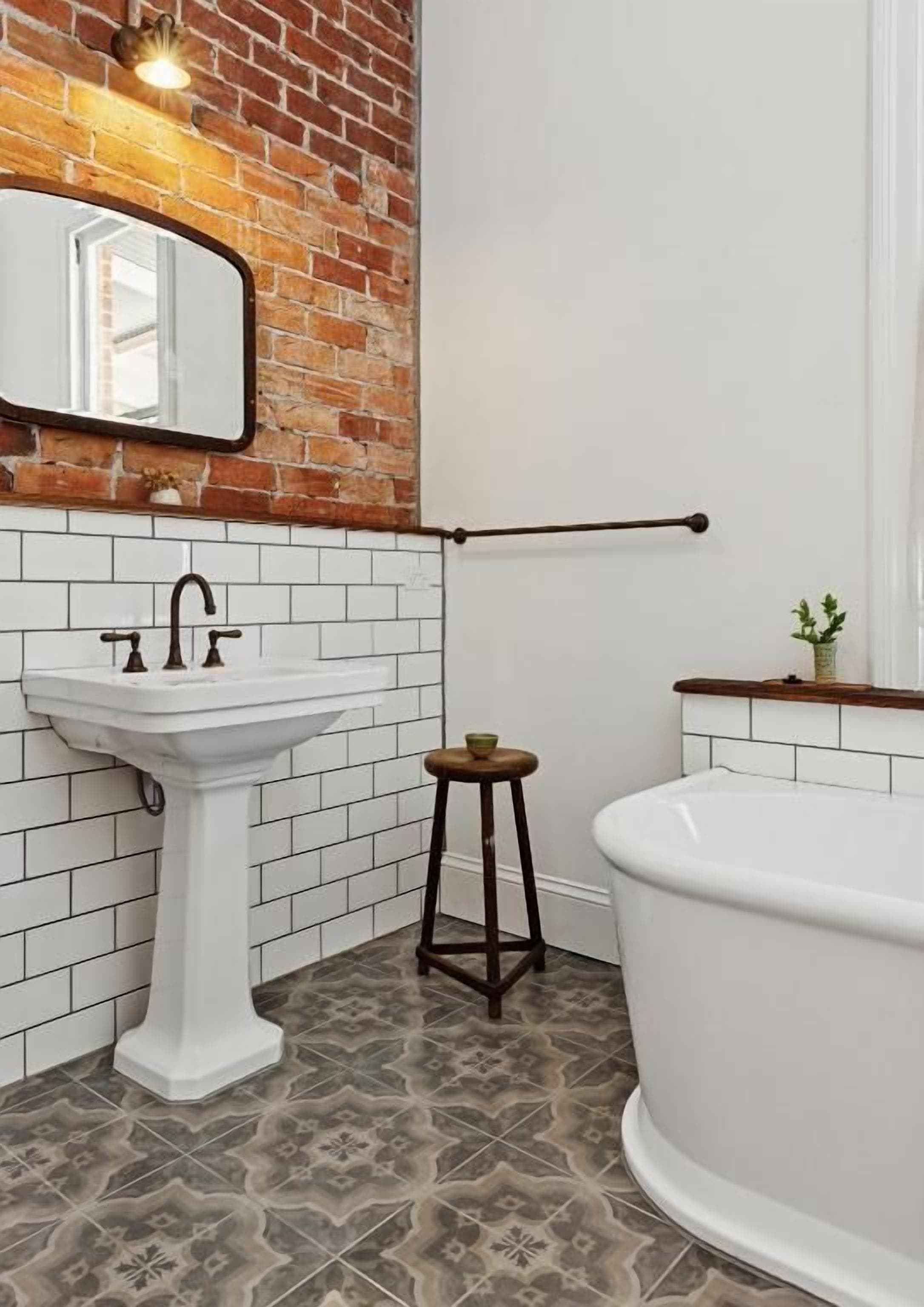 A bathroom with a white pedestal sink, a white bathtub, and a wooden stool.