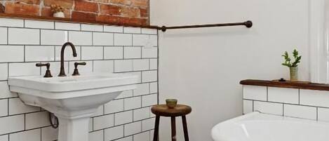 A bathroom with a white pedestal sink, a white bathtub, and a wooden stool.