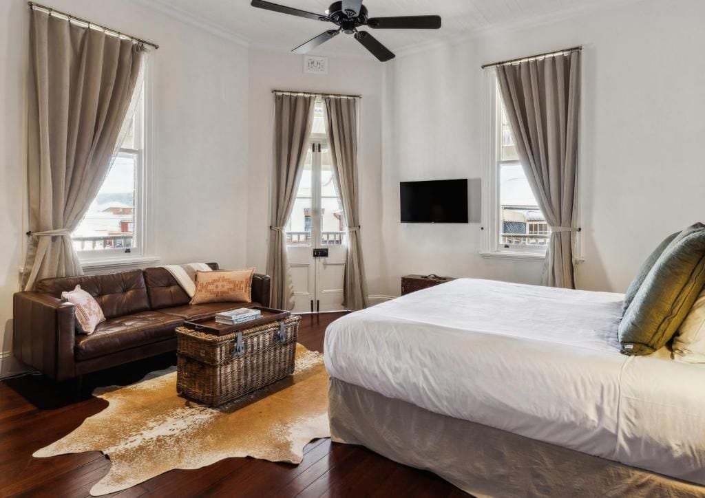 Een slaapkamer met een groot bed, een leren bank, een televisie en een plafondventilator.