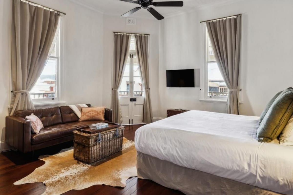 Quarto com uma cama grande, um sofá de couro, uma televisão e um ventilador de teto.