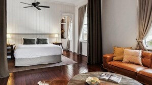 Quarto de hotel com cama, sofá de couro, mesa de centro e ventilador de teto.