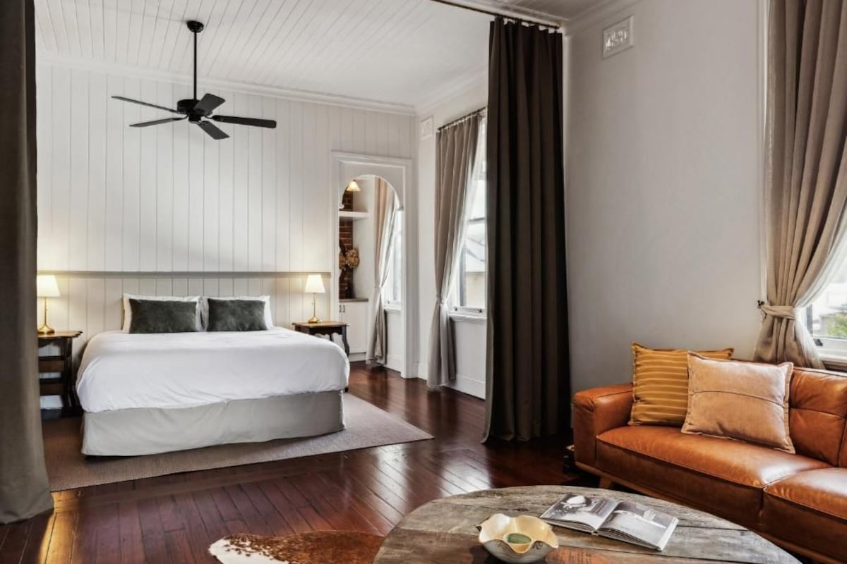 Quarto de hotel com cama, sofá de couro, mesa de centro e ventilador de teto.