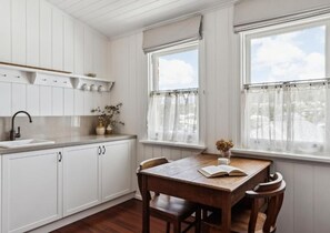 A kitchen with white cabinetry, a wooden table, and two windows with curtains. - Argyle Hotel Maclean (Maclean)