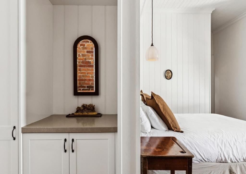 Ein Zimmer mit einem Bett, einem Nachttisch aus Holz, einer Pendelleuchte und einer Wand mit Backsteinmuster.