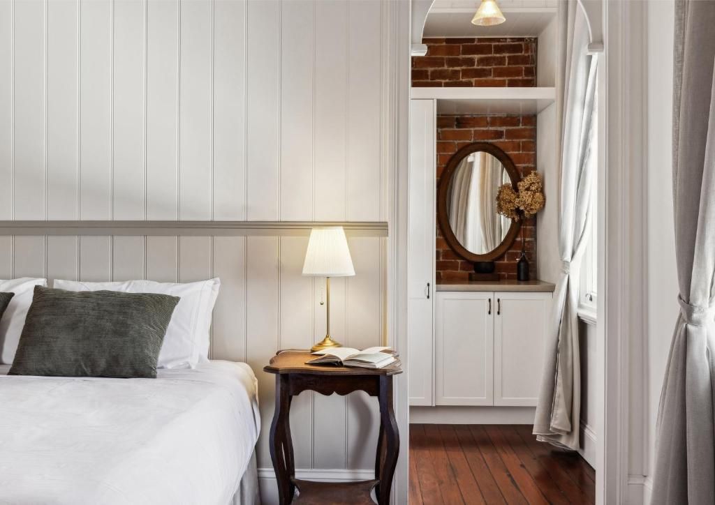 A hotel room with a bed, a bedside table with a lamp, a mirror, and a brick wall.