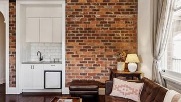 A living room with a brick wall, a brown leather sofa, a white cabinet, and a small table with a lamp.