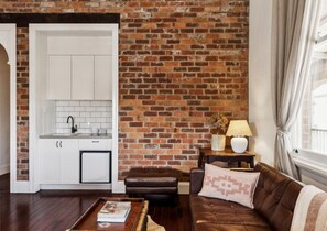 A living room with a brick wall, a brown leather sofa, a white cabinet, and a small table with a lamp.
