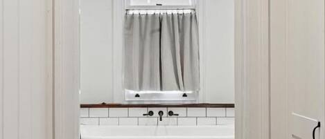 Un baño con una bañera blanca, un ventanal con cortinas y baldosas de suelo estampadas.