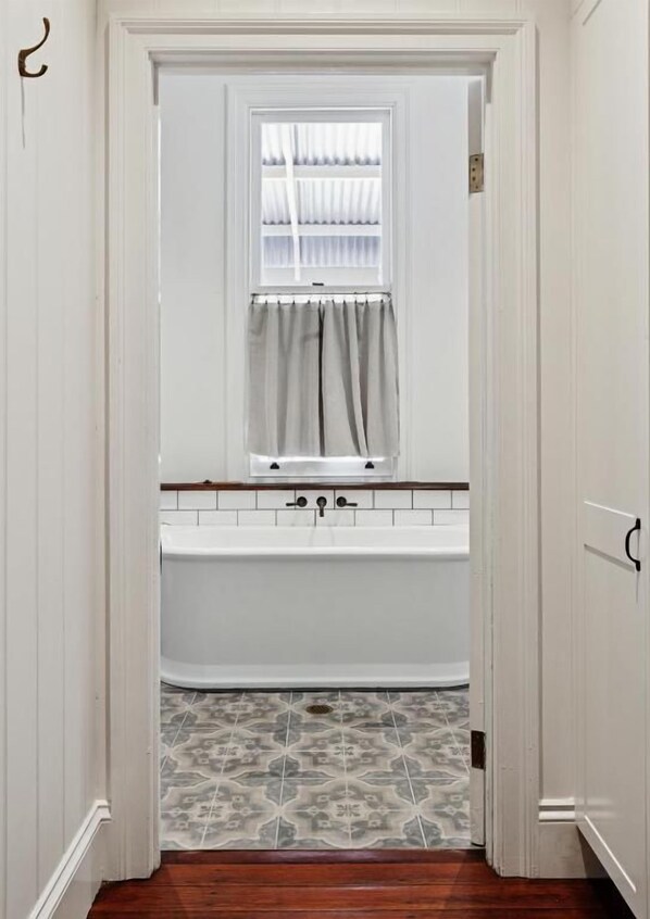 A bathroom with a white bathtub, a window with curtains, and patterned floor tiles.