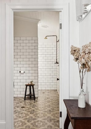 A bathroom with white subway tiles, a patterned floor, a small stool, and a vase with dried flowers. - Argyle Hotel Maclean (Maclean)