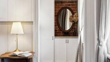 A hallway with a wooden floor, white walls, a round mirror, a table with a lamp, and a hanging light fixture.