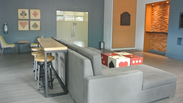 A modern lounge area with a grey sofa, wooden bar stools, and a wooden table. - One Uptown Residence BGC Stay & Work in BGC | 300Mbps WiFi (Makati City)