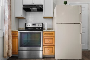 A kitchen with a stainless steel oven, wooden cabinets, a white refrigerator, and a patterned curtain. - Cozy Detroit House | 3BR Sleeps 6 Near Downtown (Detroit)