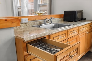 A kitchen with a granite countertop, stainless steel sink, wooden cabinets, and a microwave. - Cozy Detroit House | 3BR Sleeps 6 Near Downtown (Detroit)