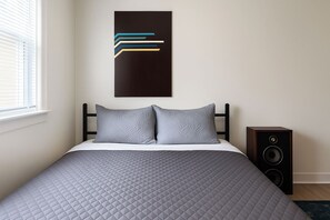 Ein Schlafzimmer mit einem Bett, Kissen, einem an der Wand befestigten abstrakten Kunstwerk und einem Lautsprecher.